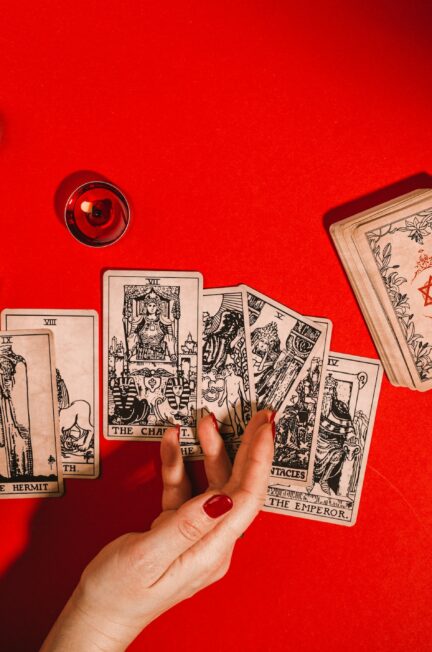 Tarot cards and female hands of fortune teller on red background